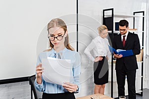 attractive young businesswoman with documents standing at modern office with colleagues