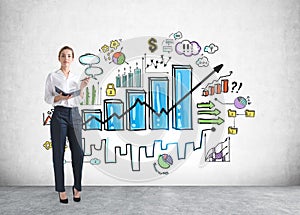 Attractive young businesswoman in formal wear holding a planner and standing near concrete wall with creative colorful bar chart