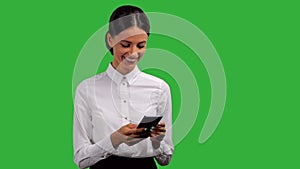 Attractive, young businesswoman standing, smiling and typing on her phone, isolated on green background