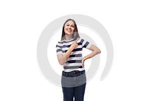 attractive young caucasian brunette woman in a striped t-shirt points with her hands to the advertising space on a white