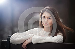 Attractive young Caucasian girl wearing a white blouse sitting on a bench in park. Beautiful brown hair teen girl