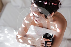 attractive young caucasian woman relaxing well in bed during morning time. Lady enjoys cup of coffee in bedroom