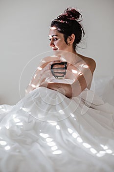 attractive young caucasian woman relaxing well in bed during morning time. Lady enjoys cup of coffee in bedroom