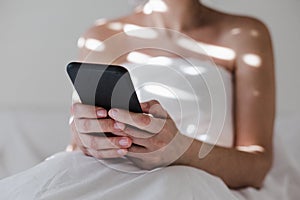 attractive young caucasian woman relaxing well in bed during morning time. Lady using mobile phone in bedroom