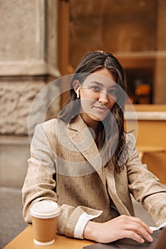 Attractive young caucasian woman is sitting in cafe with laptop on coffee break outdoors.