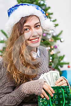 Attractive young Caucasian woman taking dollars cash in hands from green bag at Christmas eve