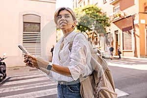 Attractive young caucasian woman is using internet outside standing on city street.