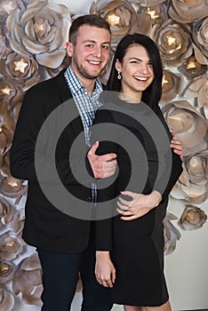 An attractive young couple on a background of a wall decorated with artificial flowers.