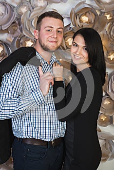An attractive young couple on a background of a wall decorated with artificial flowers.