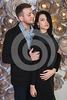 An attractive young couple on a background of a wall decorated with artificial flowers.