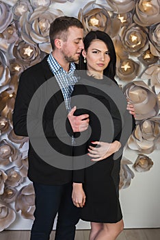 An attractive young couple on a background of a wall decorated with artificial flowers.