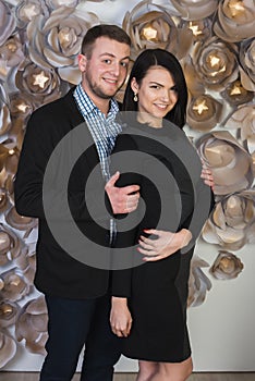 An attractive young couple on a background of a wall decorated with artificial flowers.