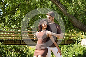 Attractive young couple dancing sensual bachata in an outdoor park surrounded by greenery. Latin dance concept, sensual, folklore