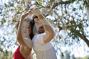 Attractive young couple dancing sensual bachata in an outdoor park, surrounded by trees, next to a river. Latin, sensual,