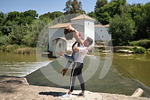 Attractive young couple dancing sensual bachata on a stone floor, in an outdoor park, next to a river. Latin dance concept,