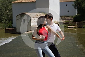 Attractive young couple dancing sensual bachata on a stone floor, in an outdoor park, next to a river. Latin dance concept,