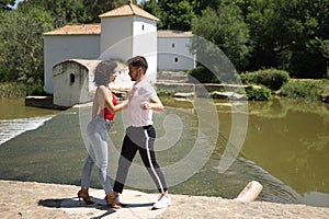 Attractive young couple dancing sensual bachata on a stone floor, in an outdoor park, next to a river. Latin dance concept,