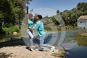 Attractive young couple dancing sensual bachata on a stone floor, in an outdoor park, next to a river. Latin dance concept,