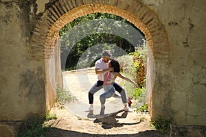 Attractive young couple dancing sensual bachata under an ancient stone arch in an outdoor park. Latin, sensual, folkloric, urban