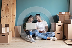 Attractive young couple looking decoration ideas with laptop while taking a break sitting on the floor at home