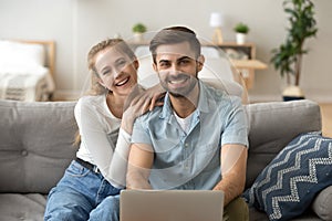 Attractive young couple using pc sitting on couch at home