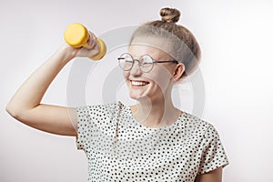 Attractive young cute woman laughing and holding dumbell. Studio shot.