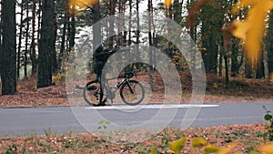 Attractive young cyclist in cycling clothes, black helmet and sports sunglasses doing `dab` pose in autumn forest. Happy handsome