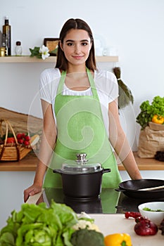 An attractive young dark-haired woman preparing soup by new keto recipe while standing and smiling in the kitchen