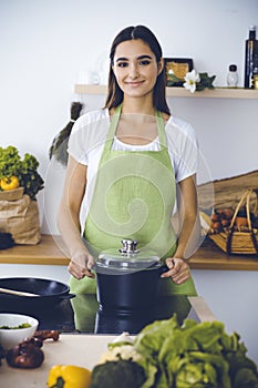 An attractive young dark-haired woman preparing soup by new keto recipe while standing and smiling in the kitchen