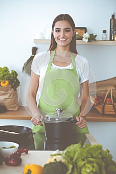 An attractive young dark-haired woman preparing soup by new keto recipe while standing and smiling in the kitchen