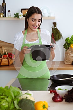 An attractive young dark-haired woman preparing soup by new keto recipe while standing and smiling in the kitchen