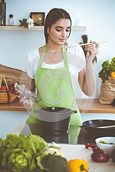 An attractive young dark-haired woman preparing soup by new keto recipe while standing and smiling in the kitchen