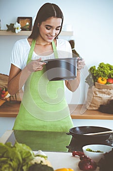 An attractive young dark-haired woman preparing soup by new keto recipe while standing and smiling in the kitchen