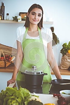 An attractive young dark-haired woman preparing soup by new keto recipe while standing and smiling in the kitchen