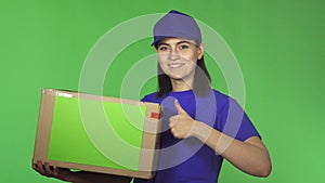 Attractive young delivery woman showing thumbs up holding cardboard box