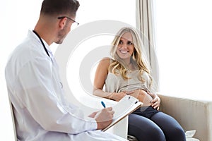 Attractive young doctor giving a routine check to beautiful pregnanat woman in medical office.