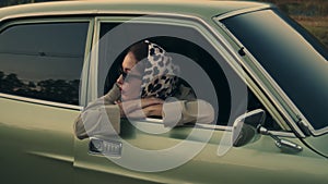 Attractive young elegant woman leans on window of her retro car.