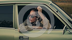 Attractive young elegant woman leans on window of her retro car.
