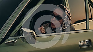 Attractive young elegant woman puts a lipstick in her retro car.