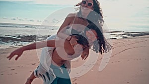 Attractive young and energetic couple having fun on the beach. Woman piggyback riding a man and laughing. Sea Summer