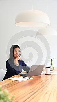 Attractive young entrepreneur sitting in modern office with statistics document beside her