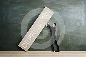 Attractive young european businessman stopping wooden block with crisis, depression and inflation concept on chalkboard wall