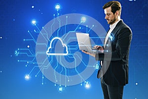 Attractive young european businessman using laptop with creative digital circuit cloud on blue background. Data storage, server