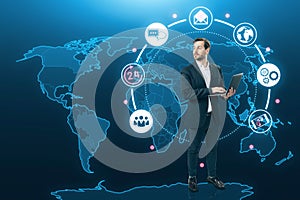 Attractive young european businessman using laptop with creative global map hologram with 24 7 online support on blue background.