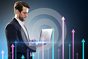 Attractive young european businessman using laptop with various growing arrows on gray background. Growth, future and performance