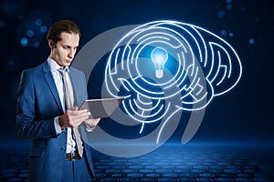 Attractive young european businessman using tablet with abstract digital light bulb with human brain inside glowing on blurry blue