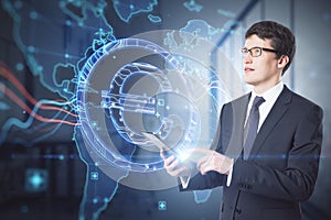 Attractive young european businessman using tablet with abstract glowing map and euro sign hologram on blurry office interior