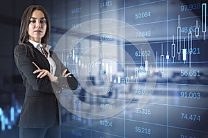 Attractive young european businesswoman with folded arms standing in blurry office interior with glowing forex chart and big data