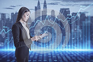 Attractive young european businesswoman using tablet with abstract glowing blue business graph hologram on blurry city background