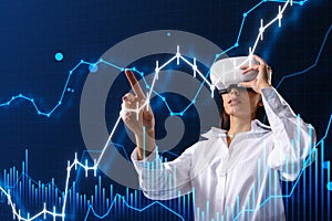 Attractive young european businesswoman with VR glasses using glowing and growing business chart on blurry blue background.